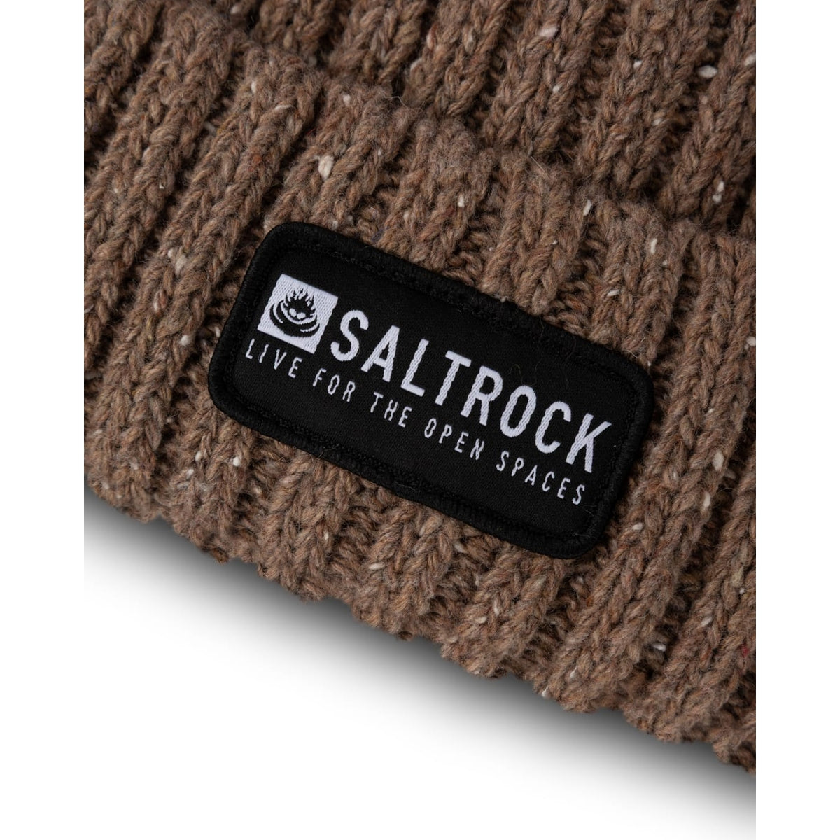 Close-up view of an adults Saltrock knitted Heritage beanie in brown, with a ribbed, fleck outer fabric, soft faux fur lining and a turn back hem with a black logo patch.