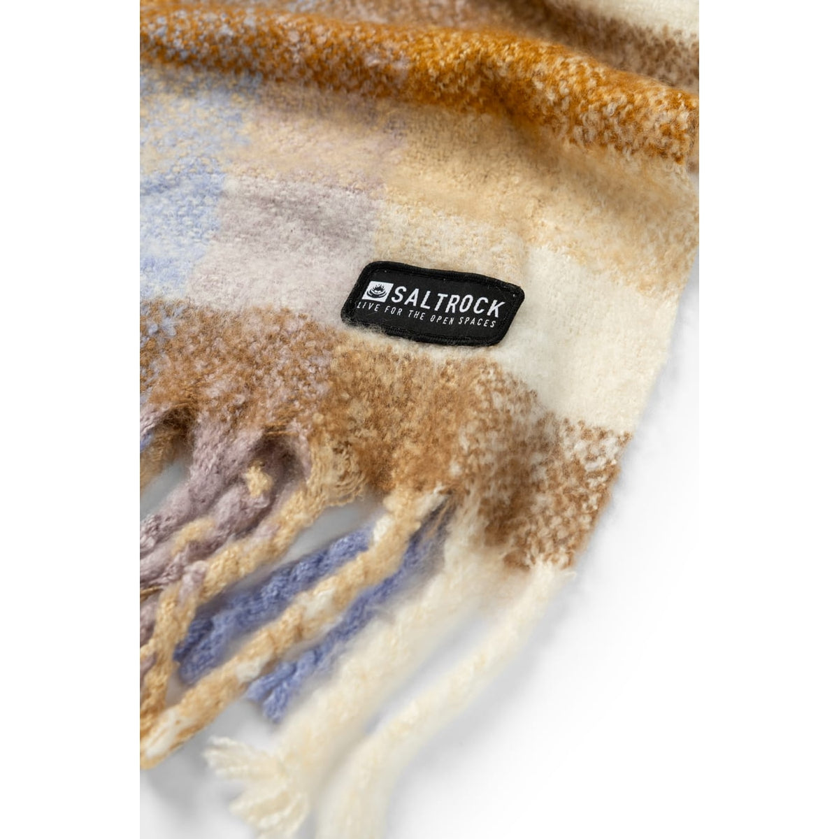 Close-up view of a Saltrock Harvest scarf in a check pattern of brown, cream and purple with tasselled ends and a black logo label.