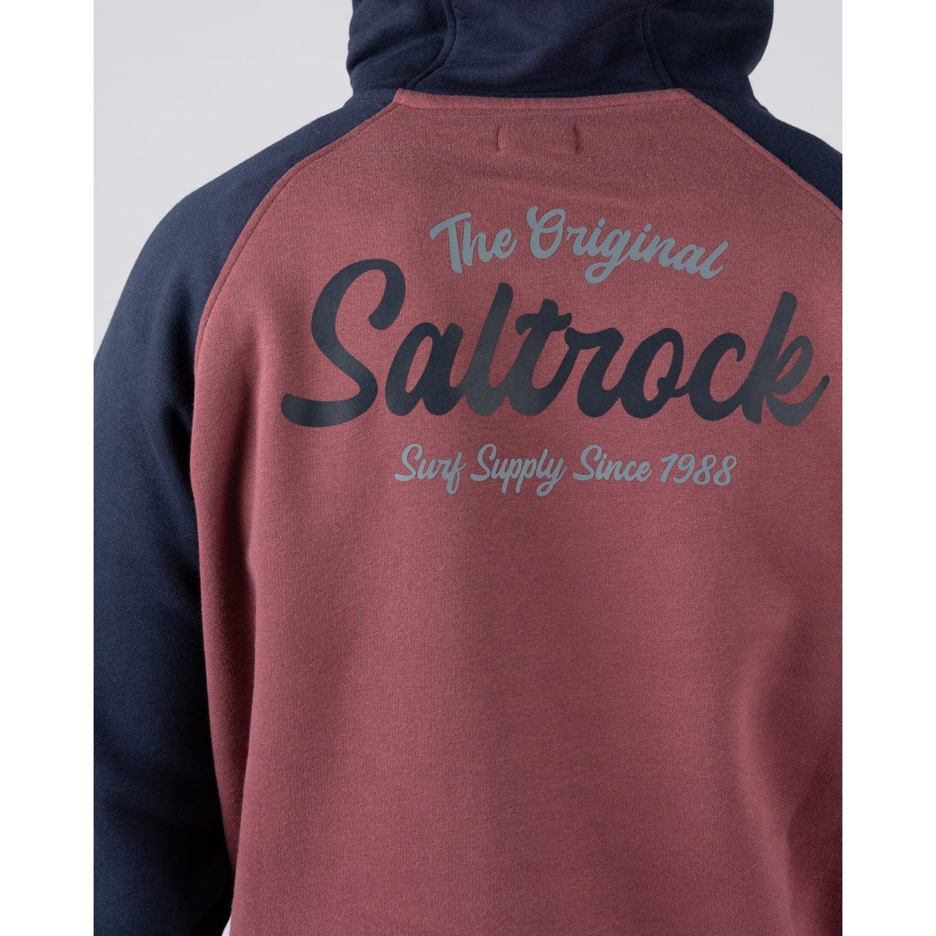Close-up view of a Saltrock men's raglan pop hoodie in dark pink with navy sleeves and hood, with large logo print on the back