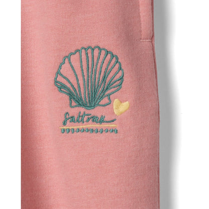 Close-up view of an embroidered shell logo on a pair of Saltrock kids Norie jogger trousers in pink