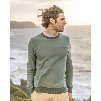 Front view of a man wearing a green Saltrock knitted Callum jumper standing by the sea.