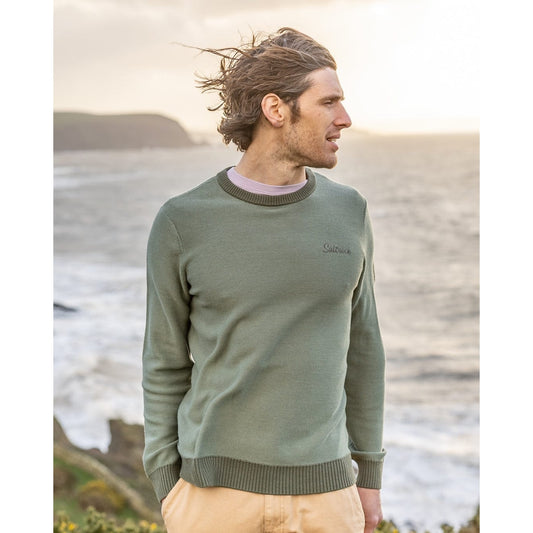 Front view of a man wearing a green Saltrock knitted Callum jumper standing by the sea.