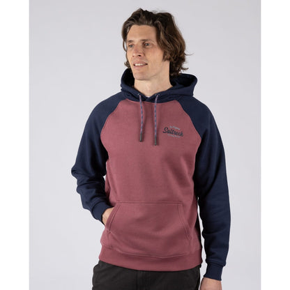 Front view of a man wearing a Saltrock Postcard Script raglan pop hoodie in dark pink with navy blue sleeves and hood