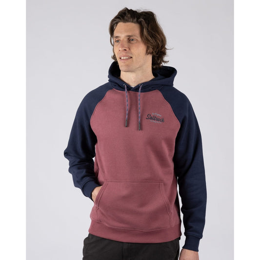 Front view of a man wearing a Saltrock Postcard Script raglan pop hoodie in dark pink with navy blue sleeves and hood