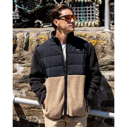 Man wearing a black and beige Saltrock Rafe zip fleece jacket standing against a stone wall.