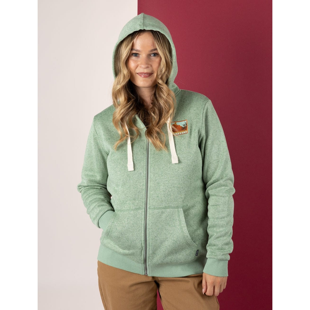 Front view of a woman wearing a Saltrock Ayden green full zip hoodie with a logo on a two-tone background