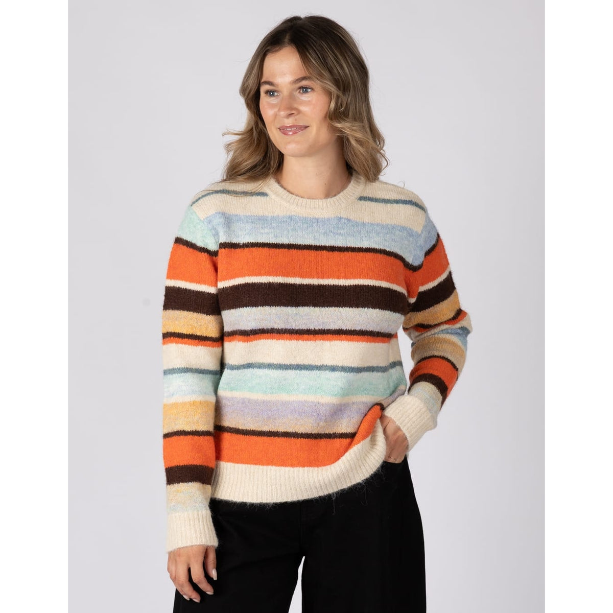 Front view of a woman wearing a Saltrock Lyris crew neck knitted jumper in an orange, cream and multicolour striped pattern.