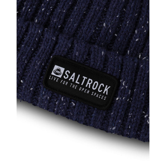 Close-up view of the logo patch, turn-up hem and ribbed knitted texture of a Saltrock adults Heritage beanie in navy with a white fleck.