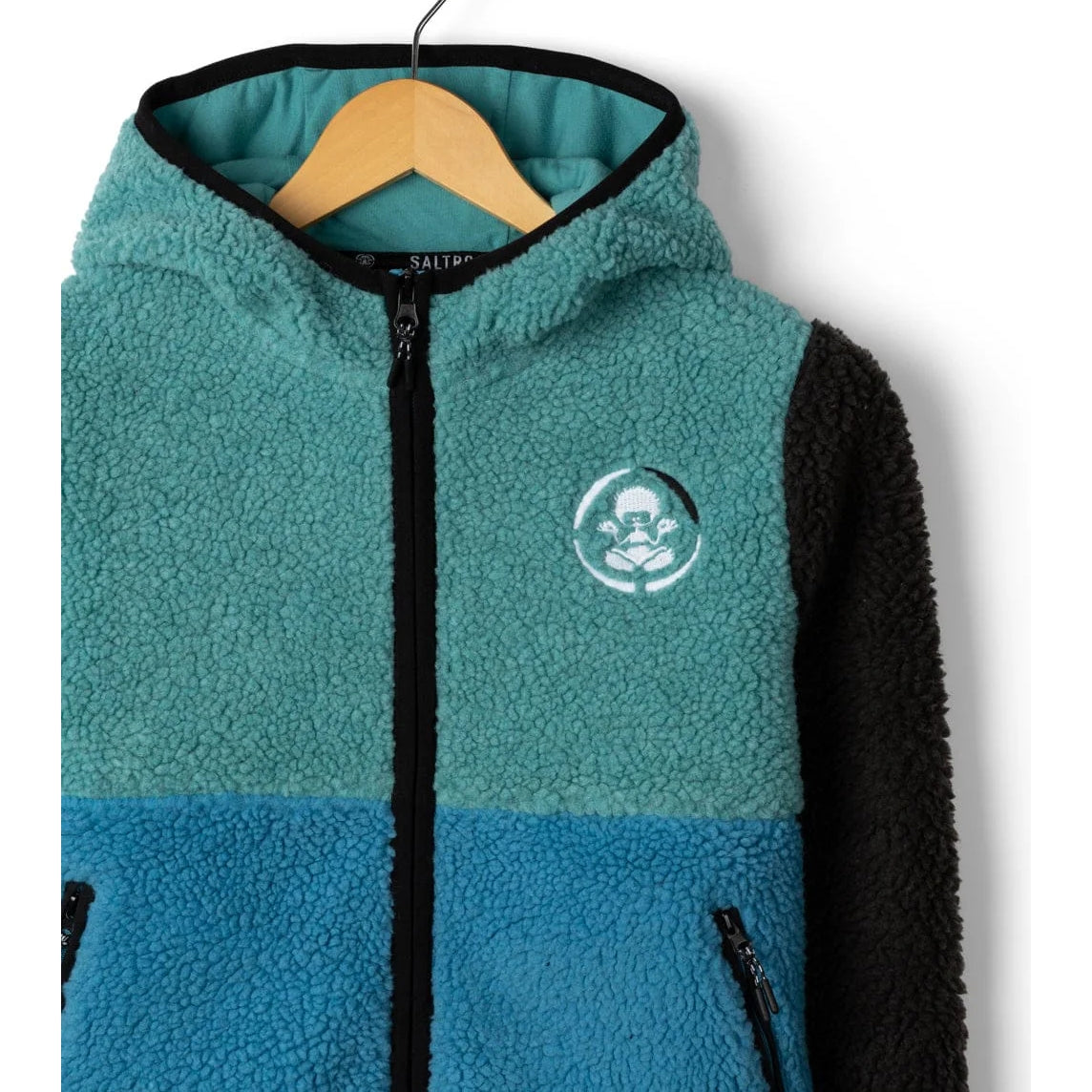 Close-up view of the front of a kids Saltrock Tok Emery fleece in blue, black and teal colour block design, with zip through front and embroidered chest logo.