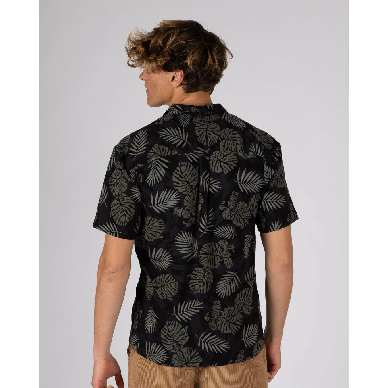 Back view of a man wearing a short sleeve Saltrock Warp Surf Resort Shirt in dark grey with a geometric and green tropical leaf print