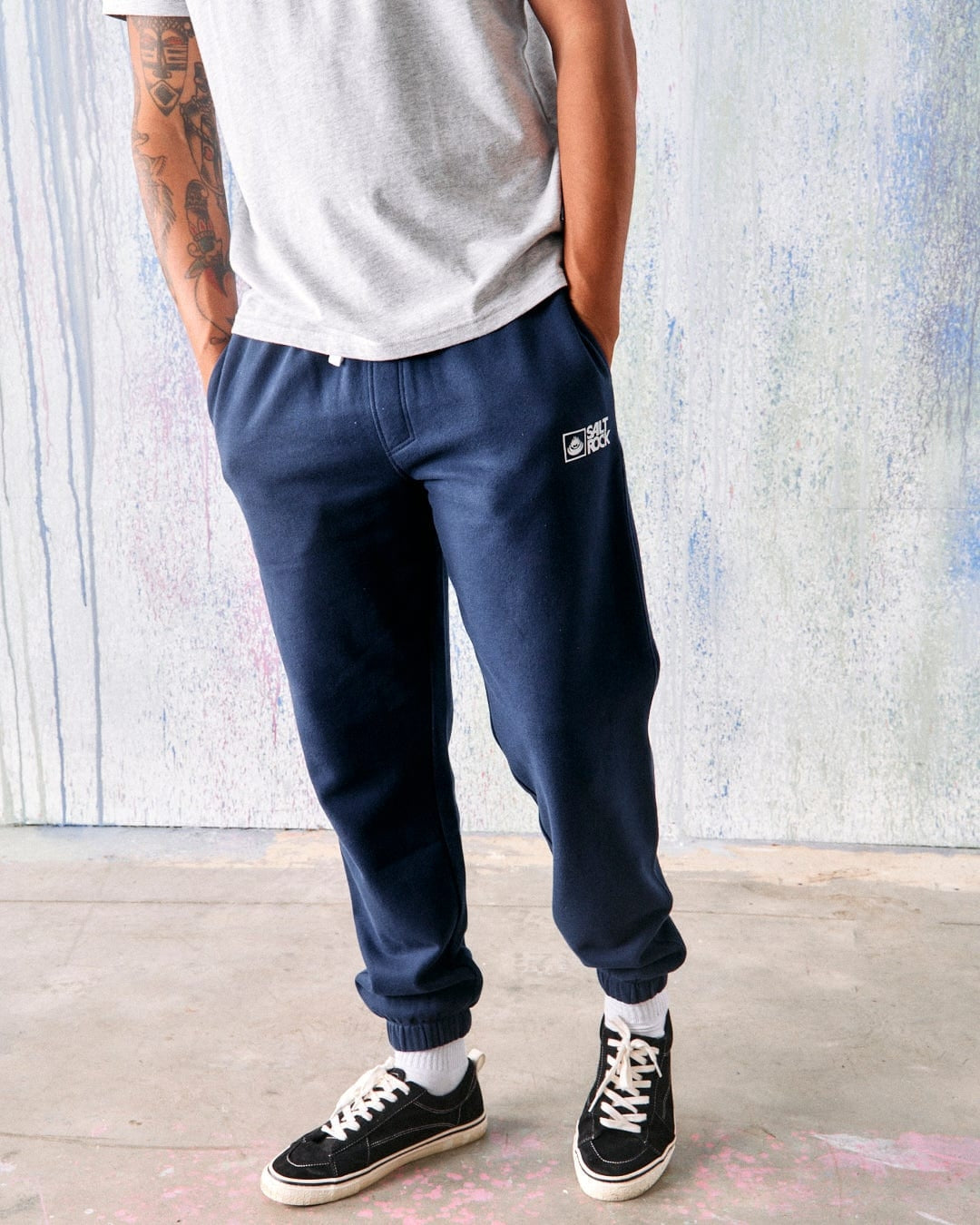 A man standing wearing Saltrock men's Original Joggers in blue marl with an elasticated waist and drawstring, along with a grey t-shirt and black sneakers.
