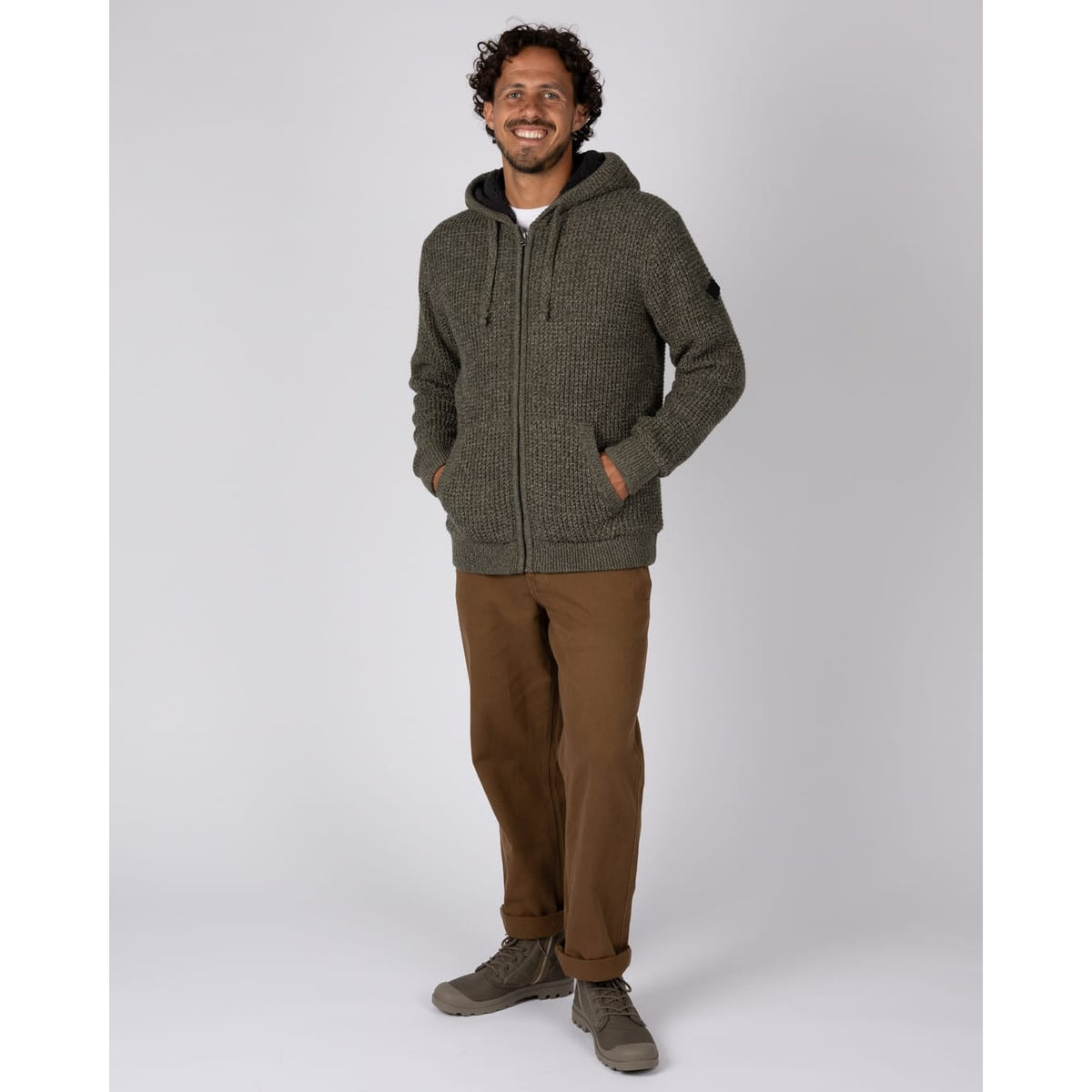 Front view of a man wearing a Saltrock dark green Markus knitted hoodie with a fluffy navy Borg lining with brown trousers.