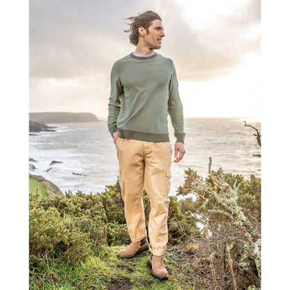 Man standing outdoors by a coastal landscape wearing a green Saltrock knitted Callum jumper