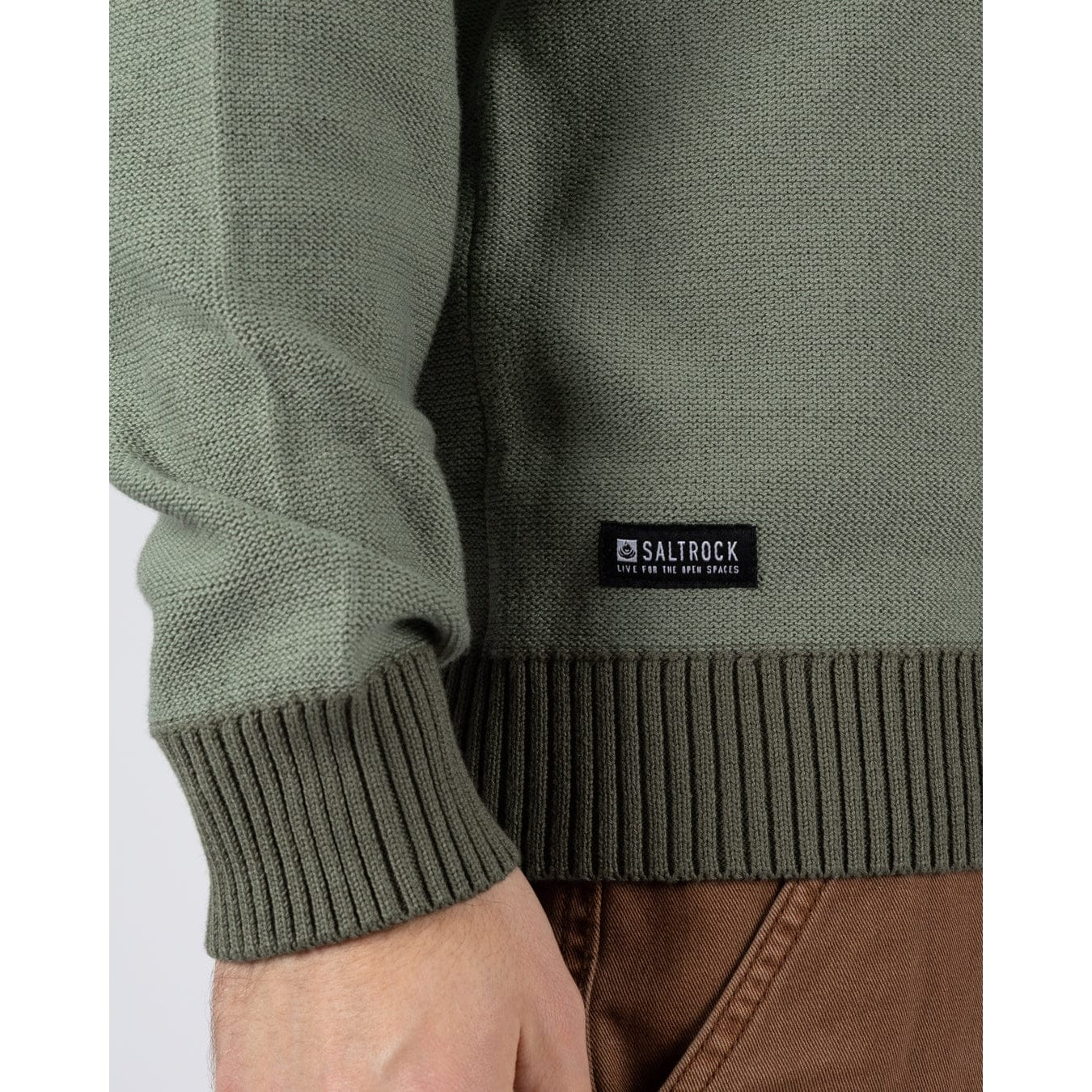Close-up view of a Saltrock knitted Callum jumper in green with ribbed cuffs, bottom hem and small black logo label