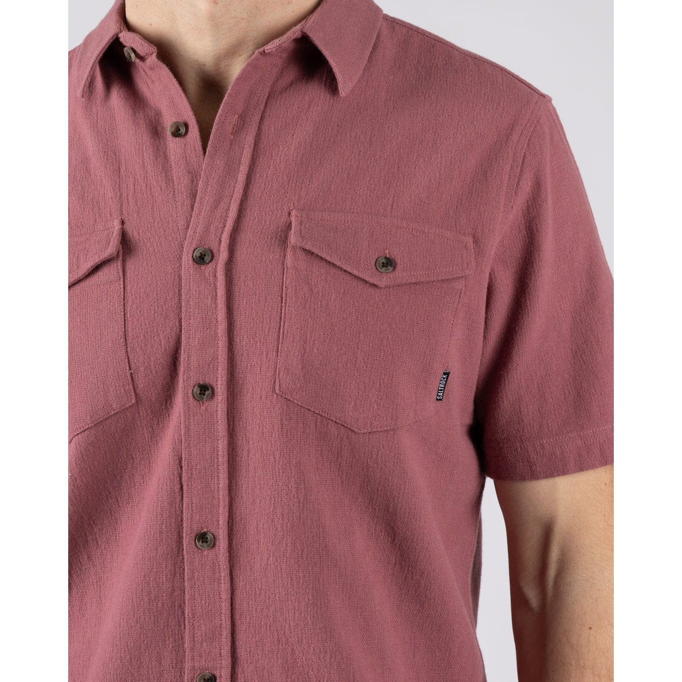 Close-up view of a button pocket on a men's Saltrock short sleeve Polperro shirt in dark pink.