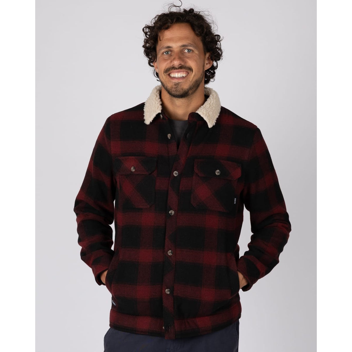 Front view of a man wearing a red and black Saltrock Fisher Borg lined shacket with two pockets on the chest and open pockets on the tummy.