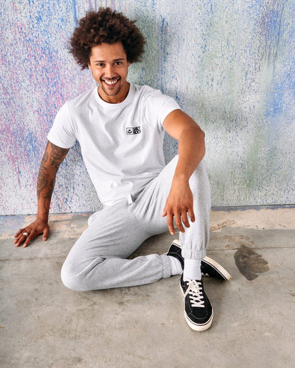 A man sat on the floor wearing a pair of mens Saltrock grey jogger sweat trousers and a white t-shirt