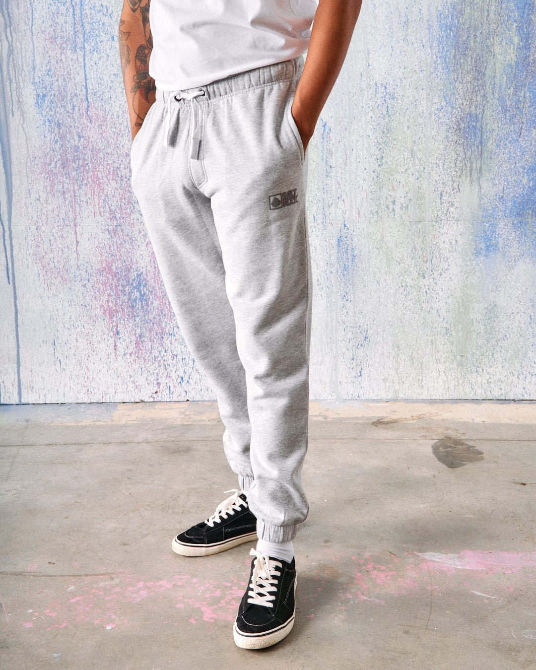 Main view of a man wearing a pair of Saltrock grey jogger trousers with a white t-shirt on a colourful painted background