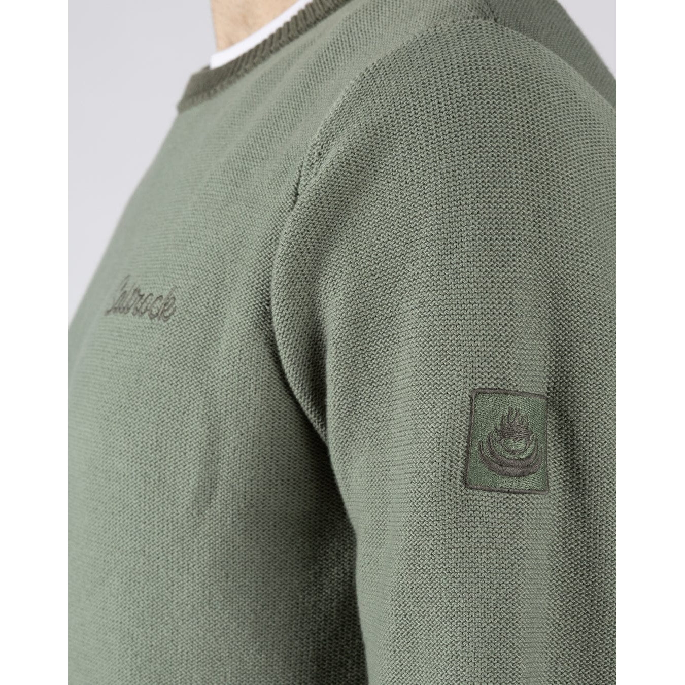 Close-up side view of a mens Saltrock green Callum knitted jumper with a small logo embroidered on the chest and a logo patch sewn on one sleeve
