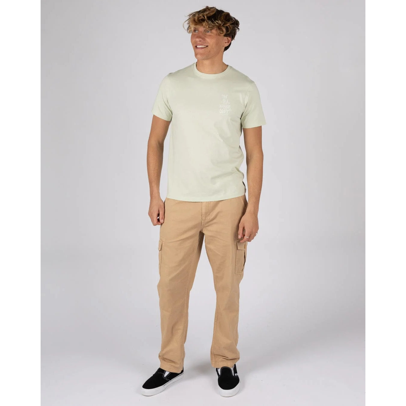 Man wearing a Saltrock short sleeve Lost Ships t-shirt in light green with tan trousers and navy shoes