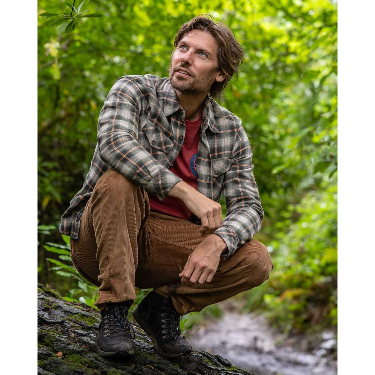 A man wearing a Saltrock Miles long sleeve flannel shirt in a green and orange check pattern, outdoors with brown trousers and black boots.
