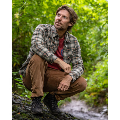 A man wearing a Saltrock Miles long sleeve flannel shirt in a green and orange check pattern, outdoors with brown trousers and black boots.