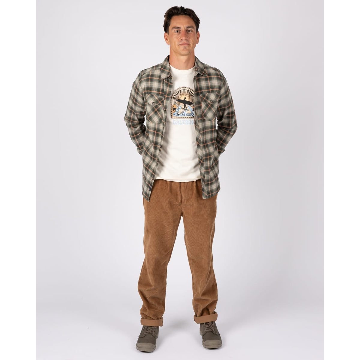 A man wearing a Saltrock long sleeve Miles flannel shirt in a green and orange check pattern over a white t-shirt with tan trousers.