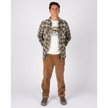 A man wearing a Saltrock long sleeve Miles flannel shirt in a green and orange check pattern over a white t-shirt with tan trousers.