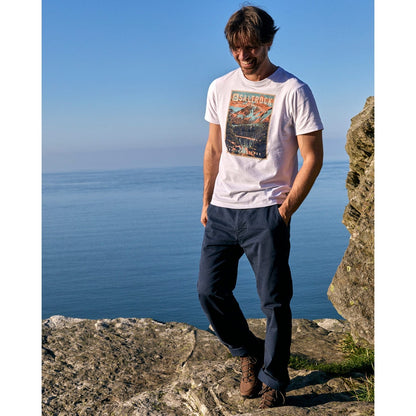 Man wearing a white Saltrock t-shirt with a graphic design, standing on a rocky outcrop by the sea.