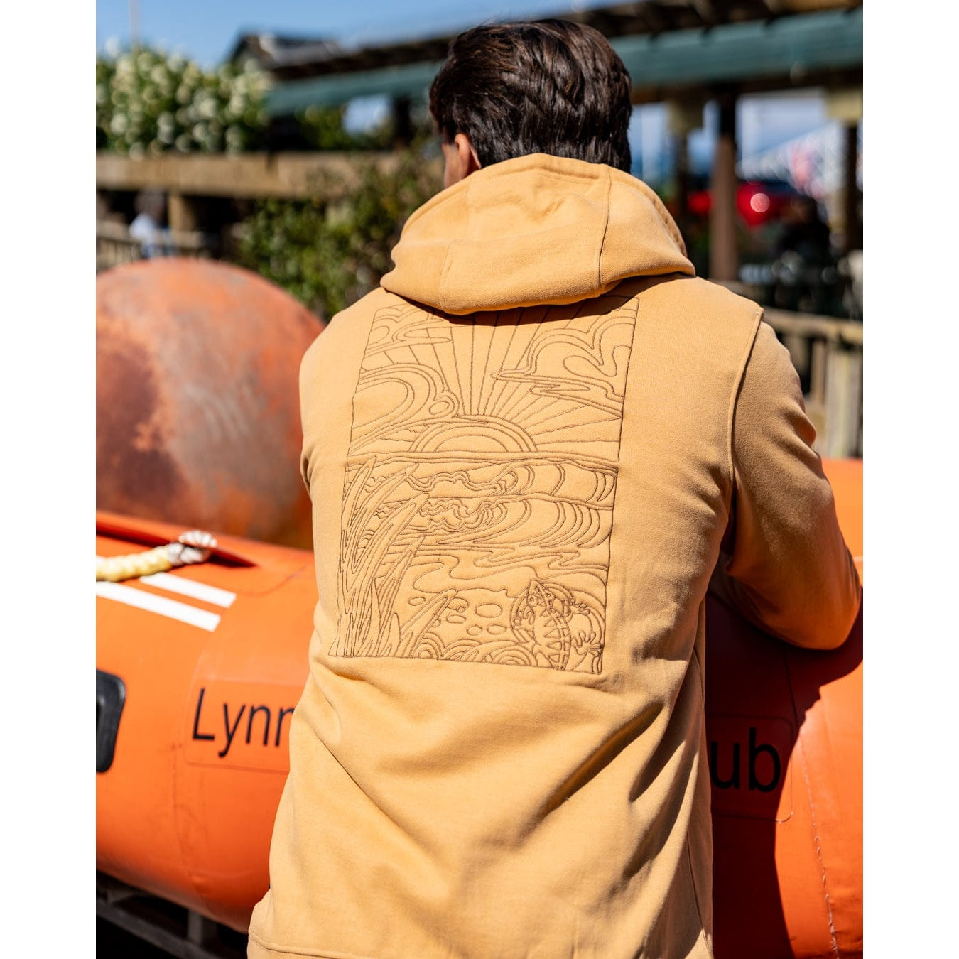 Back view of a man wearing a yellow Saltrock Open Finals Linear pop hoodie with large beach inspired embroidered design