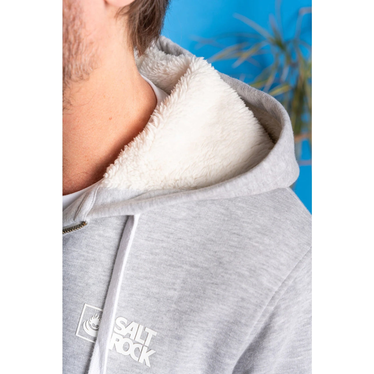 Close up of a mens grey faux fur lined hoodie with white lining and 'Salt Rock' logo on a blue background