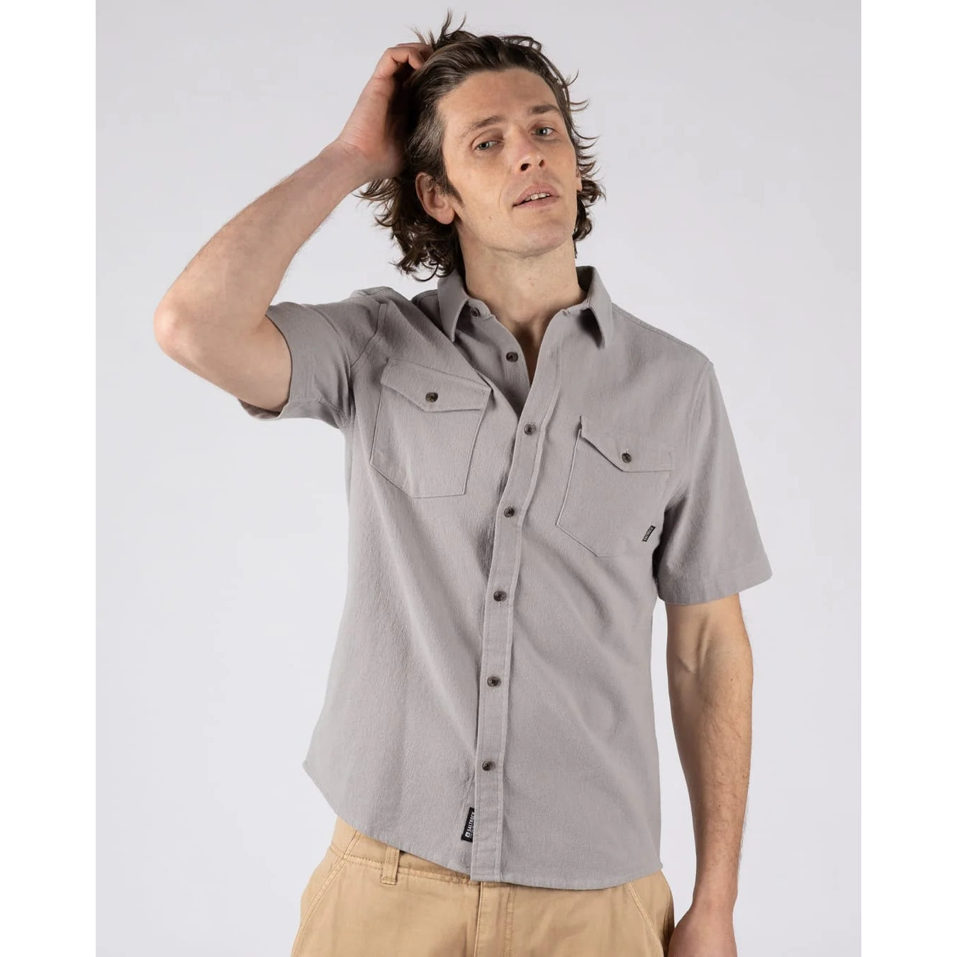 Man wearing a Saltrock short sleeve Polperro button shirt in grey with a waffle texture and two button pockets on the chest with tan trousers.