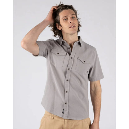 Man wearing a Saltrock short sleeve Polperro button shirt in grey with a waffle texture and two button pockets on the chest with tan trousers.