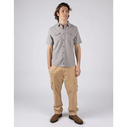 A man wearing a Saltrock short sleeve Polperro button shirt in grey with a waffle texture and two button pockets on the chest with tan trousers and brown boots.