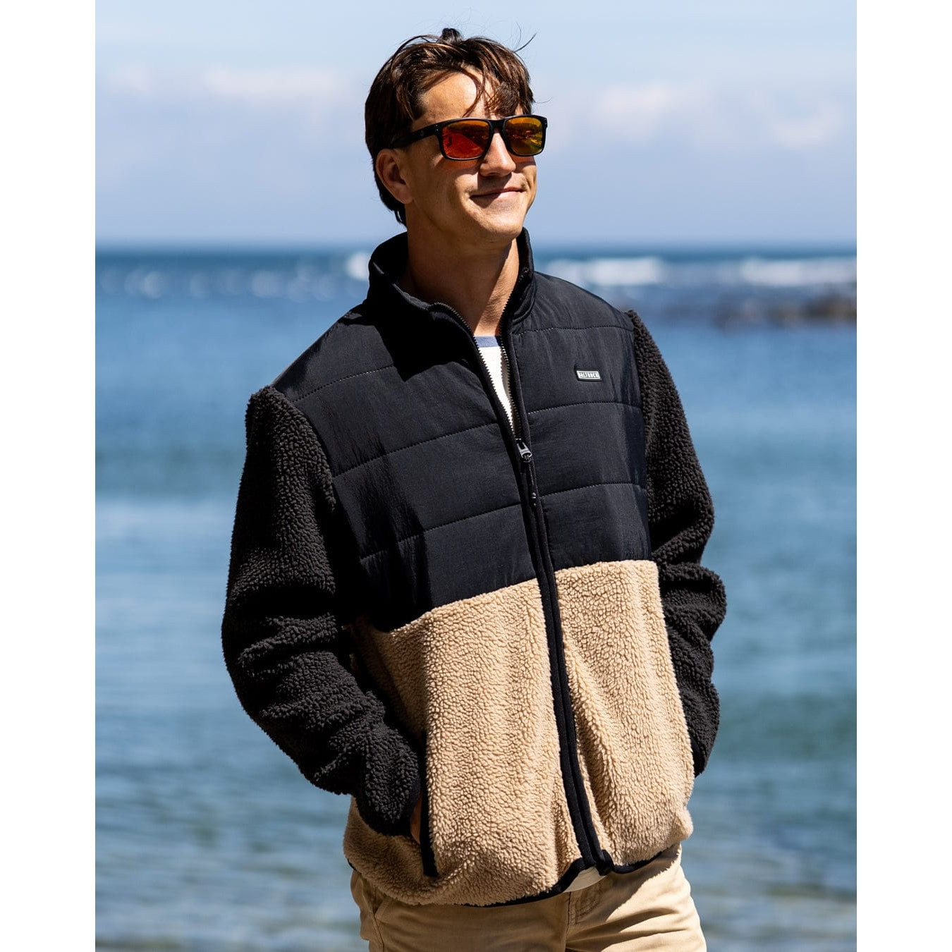 Man wearing a black and beige Saltrock Rafe fleece zip jacket by the ocean