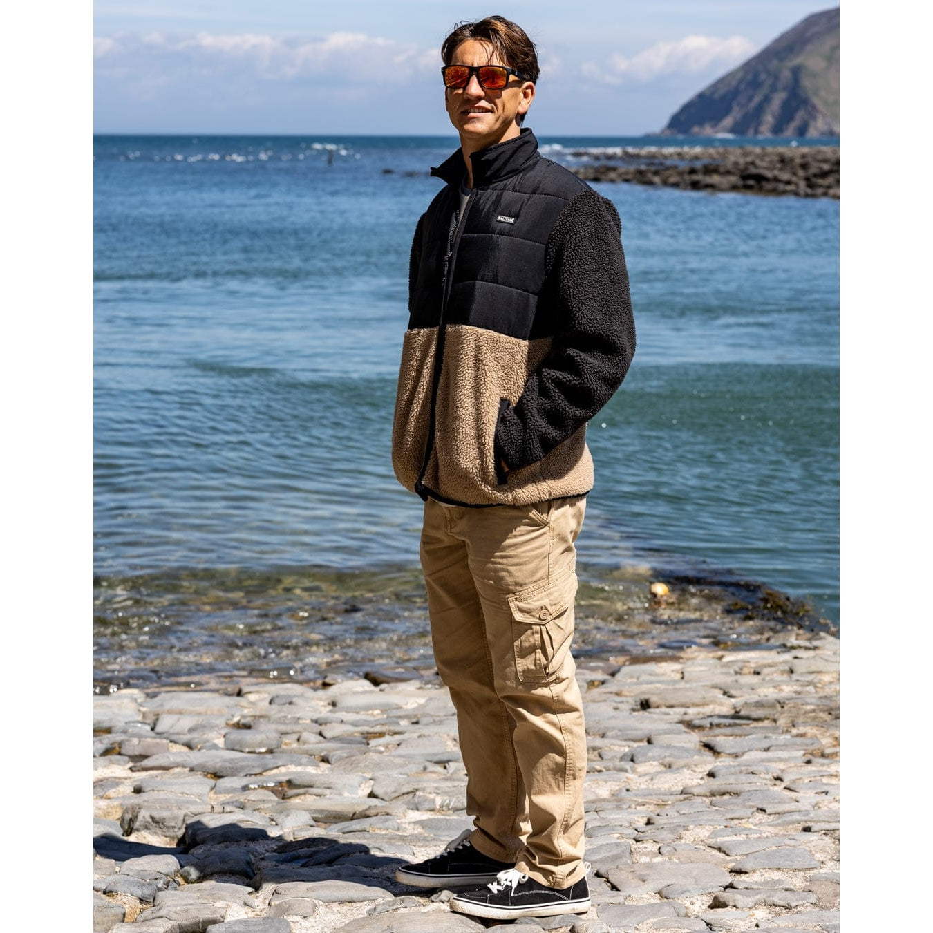 Side view of a man wearing a black and beige Saltrock Rafe zip fleece jacket standing outdoors