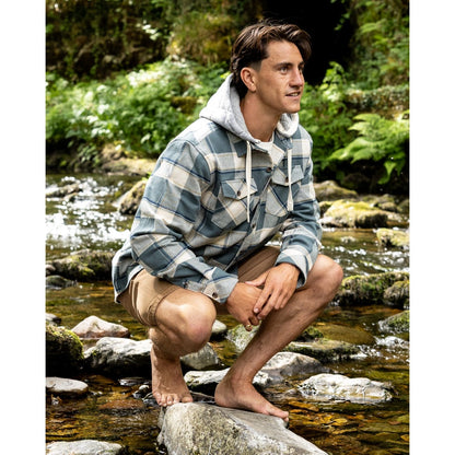 Man wearing a Saltrock Strait long sleeve check shirt in dark teal green with chest pockets, detachable hood and tan shorts outdoors