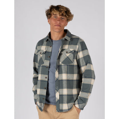 Man wearing a mens Saltrock Strait long sleeve check shirt in dark teal green with tan trousers