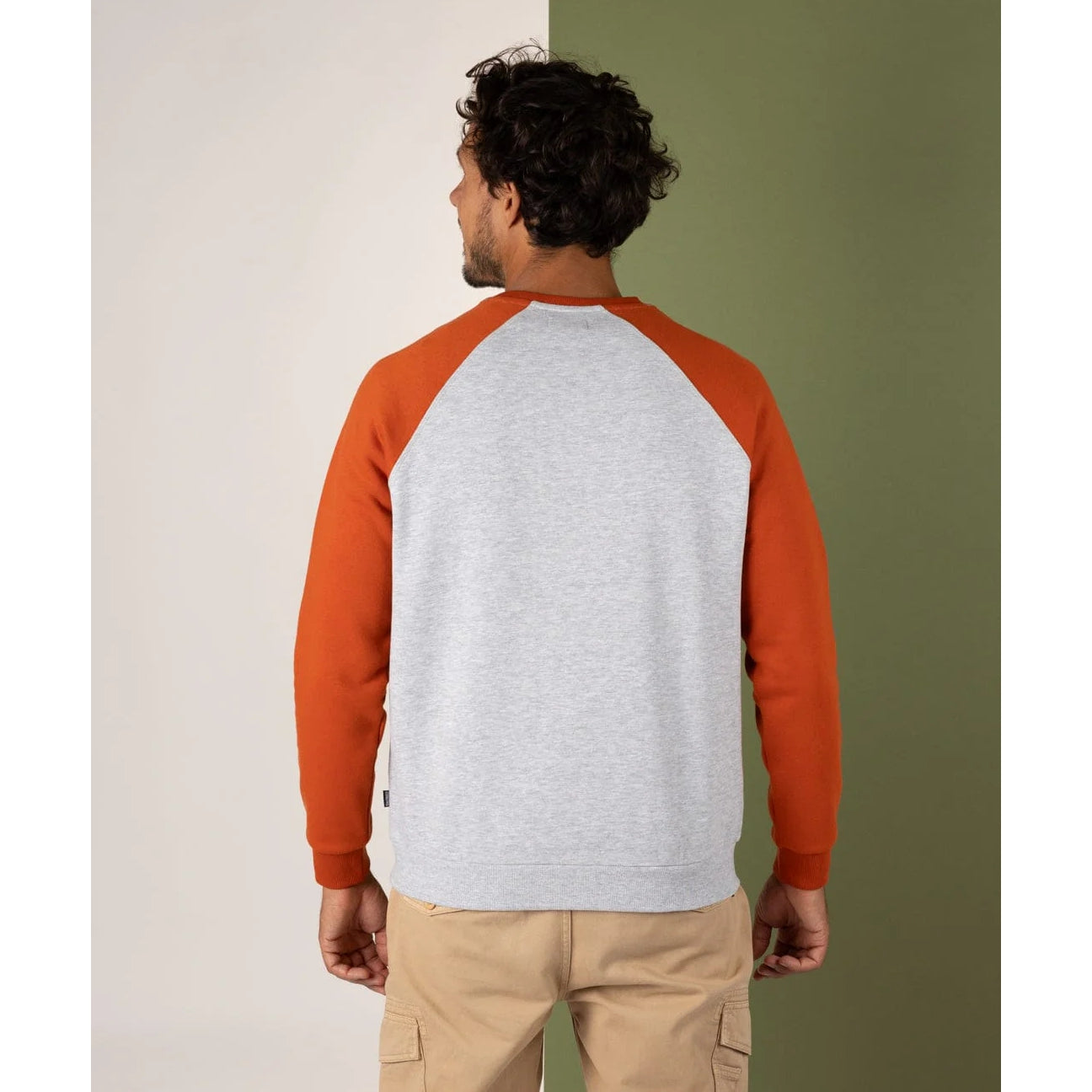 Man wearing a grey and orange baseball-style sweatshirt against a green and beige background