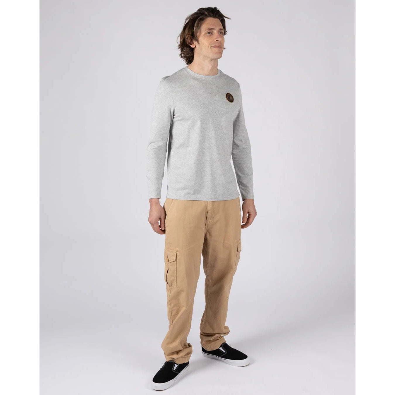 Man wearing a Saltrock Trail Badge long sleeve t-shirt in grey with a circular surf and skull themed print with tan trousers