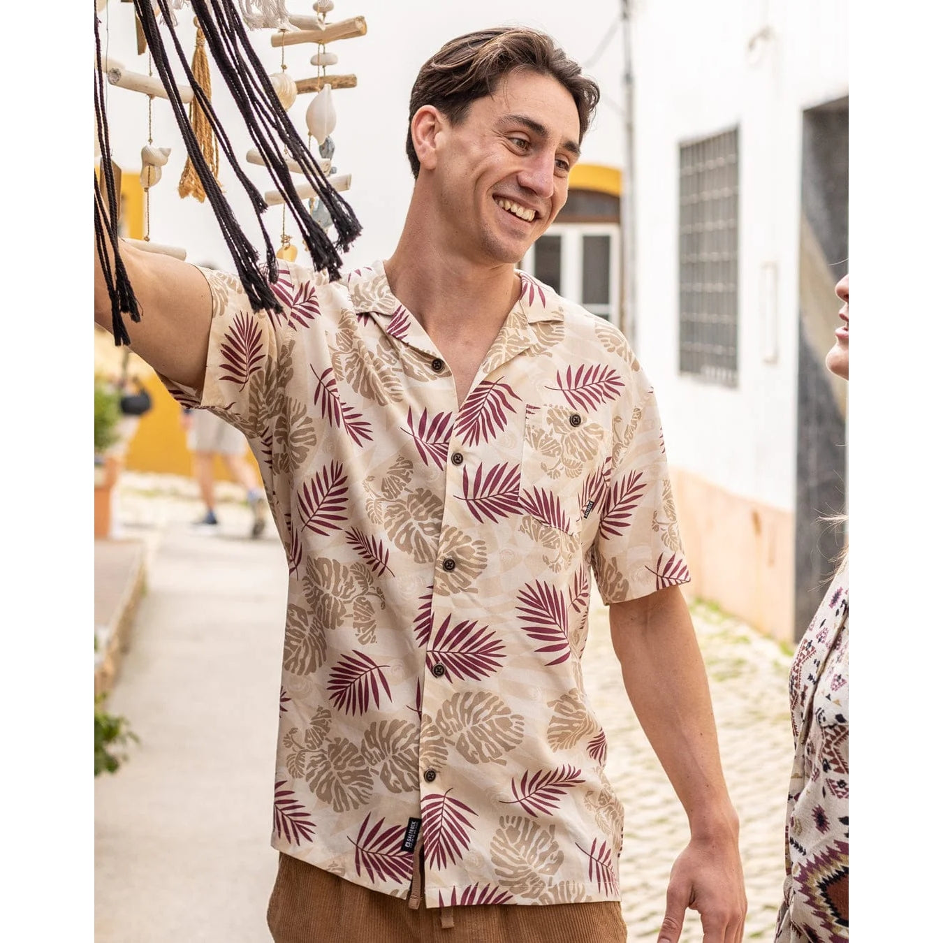 Front view of a man wearing a Saltrock short sleeve Warp Surf Resort shirt in cream with a dark red and tan tropical leaves print