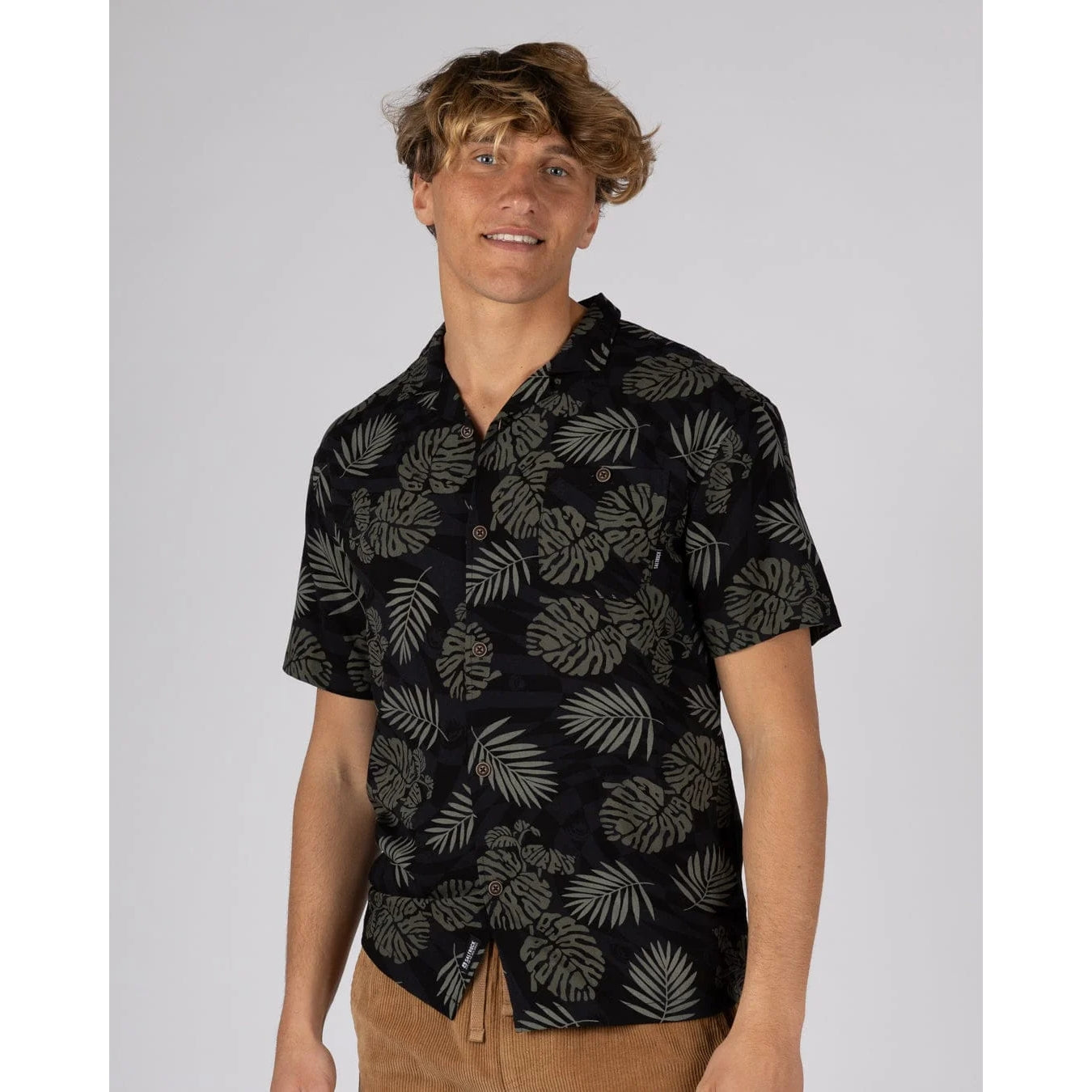 Man wearing a short sleeve Saltrock Warp Surf Resort Shirt in dark grey with a geometric and green tropical leaf print