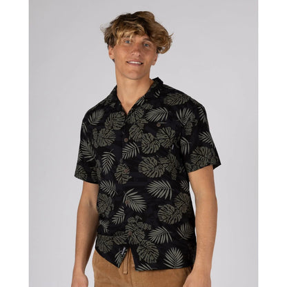 Man wearing a short sleeve Saltrock Warp Surf Resort Shirt in dark grey with a geometric and green tropical leaf print