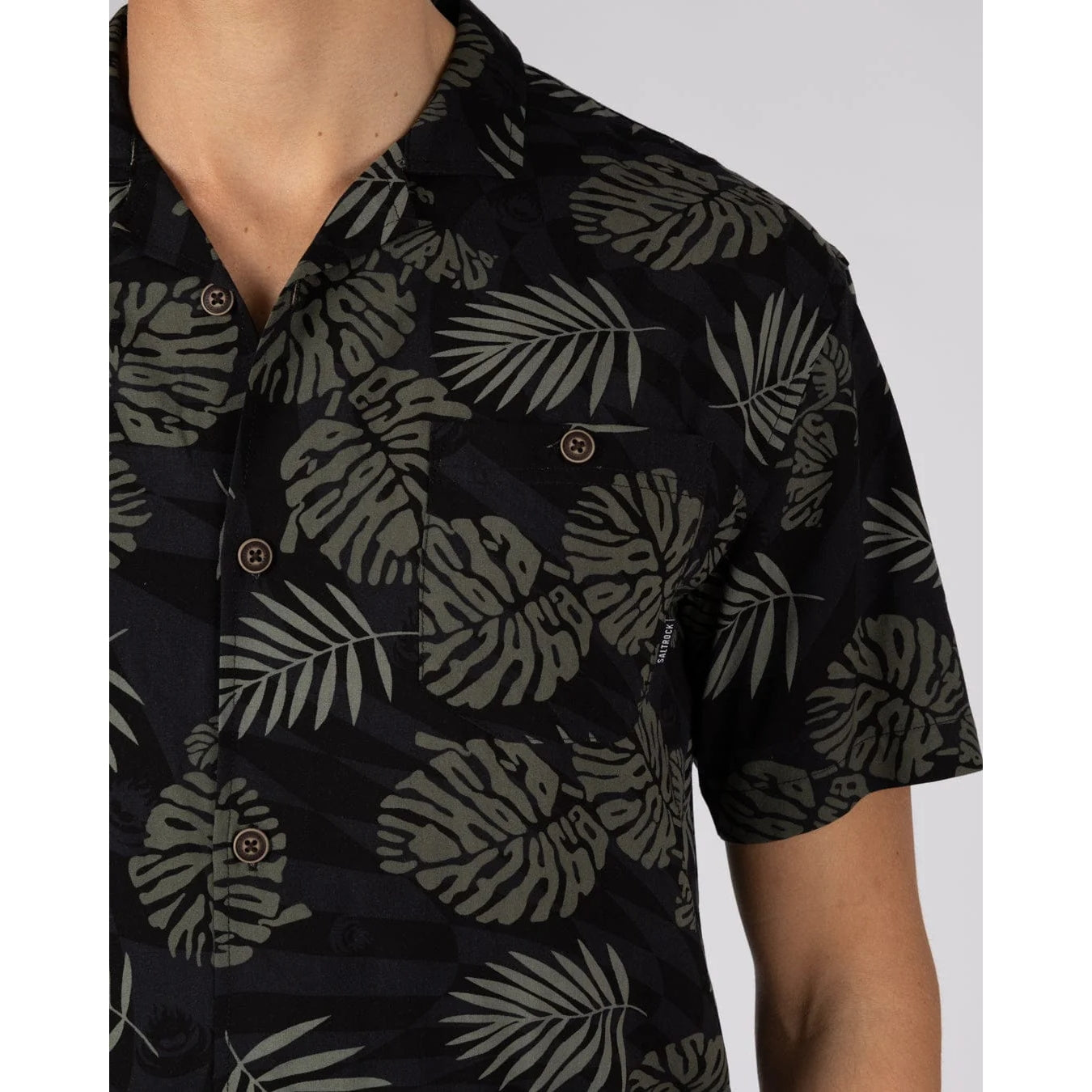 Close-up view of the chest pocket on a mens Saltrock short sleeve Warp Surf Resort shirt in dark grey with a geometric pattern and green leaf print.
