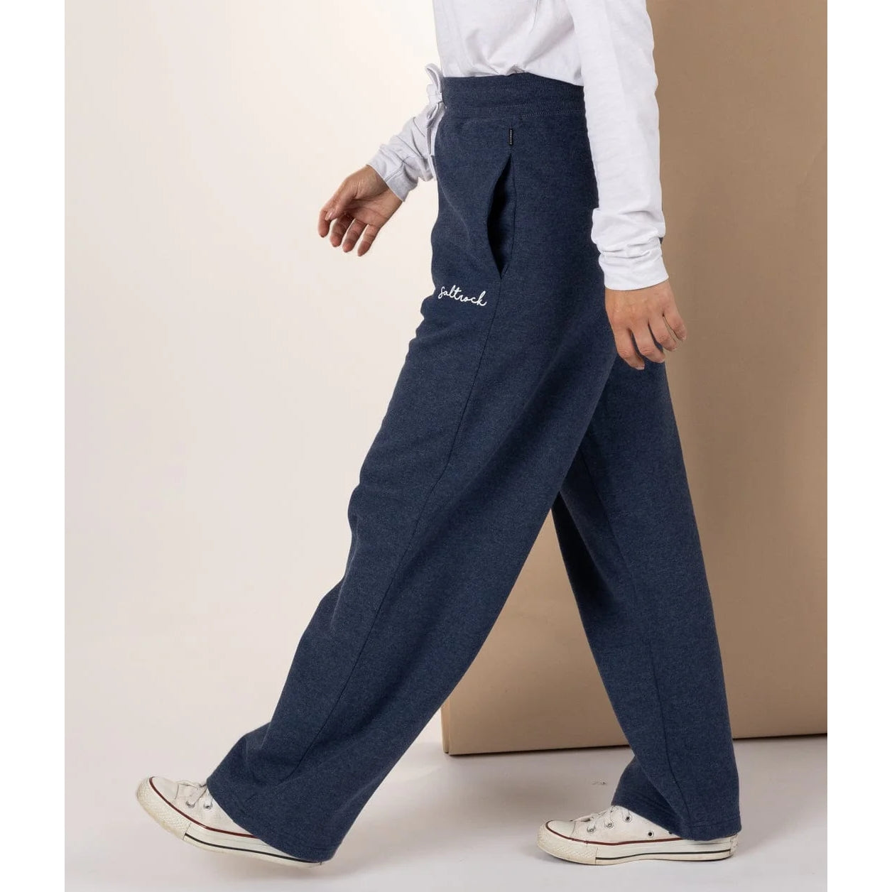 Woman wearing Saltrock blue marl sweat trousers with white logo and white sneakers on a plain background