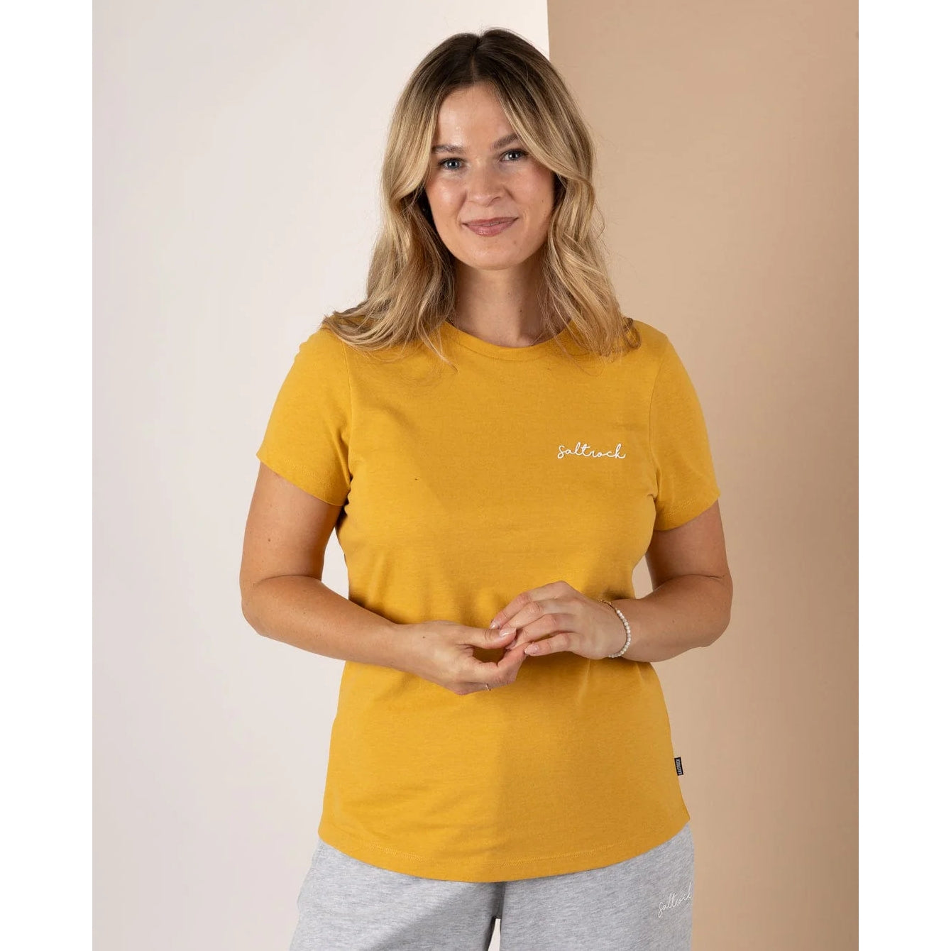 Front view of a Saltrock womens Velator t-shirt in gold yellow on smiling woman short sleeve crew neck tee with small chest logo
