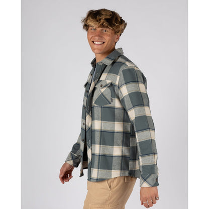 Side view of a man wearing a mens Saltrock Strait long sleeve check shirt in dark teal green with chest pockets  and tan trousers