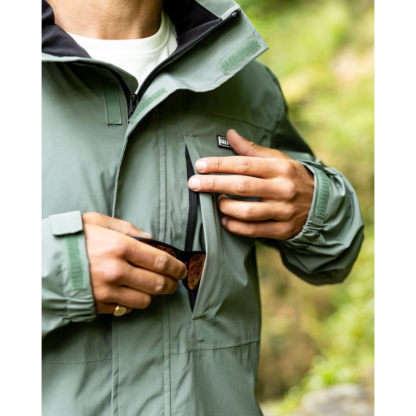 Close-up view of a chest zip pocket of a Saltrock Whistler II waterproof hooded jacket in light green outdoors