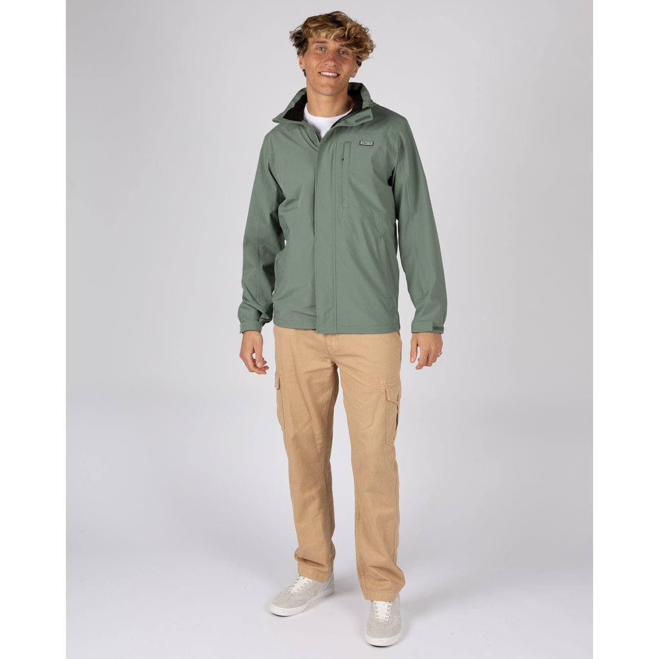 Front view of a man wearing an Saltrock Whistler II waterproof jacket in light green with tan trousers