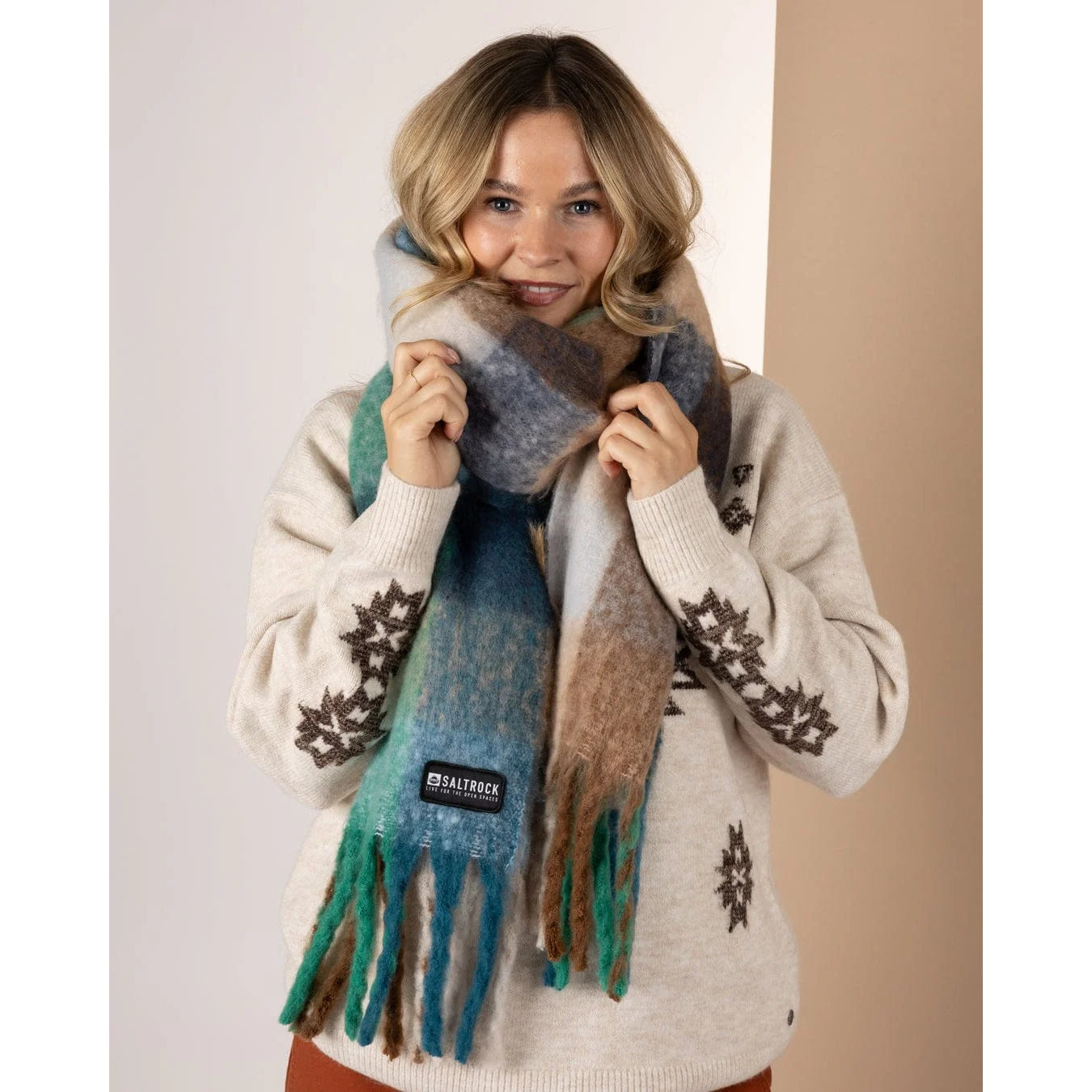 Woman wearing a Saltrock Harvest check patterned scarf in blue green and brown against a white and brown background